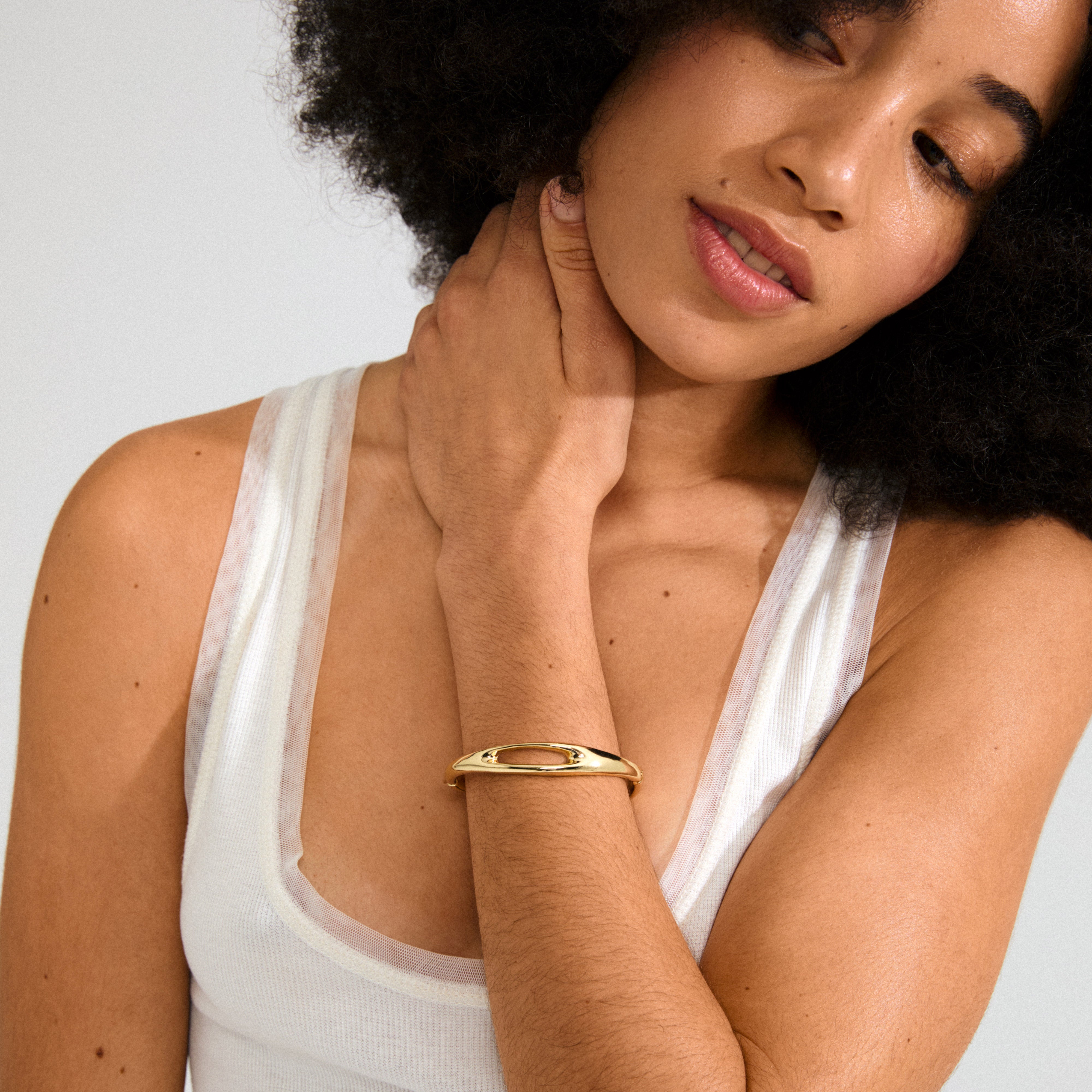 Young woman wears a white tank top and Pilgrim's 168一分钟极速赛车--|实时赛果直播视频 gold-plated FREE bangle with unique cut-out design, showcasing Scandinavian-inspired elegance and simplicity.
