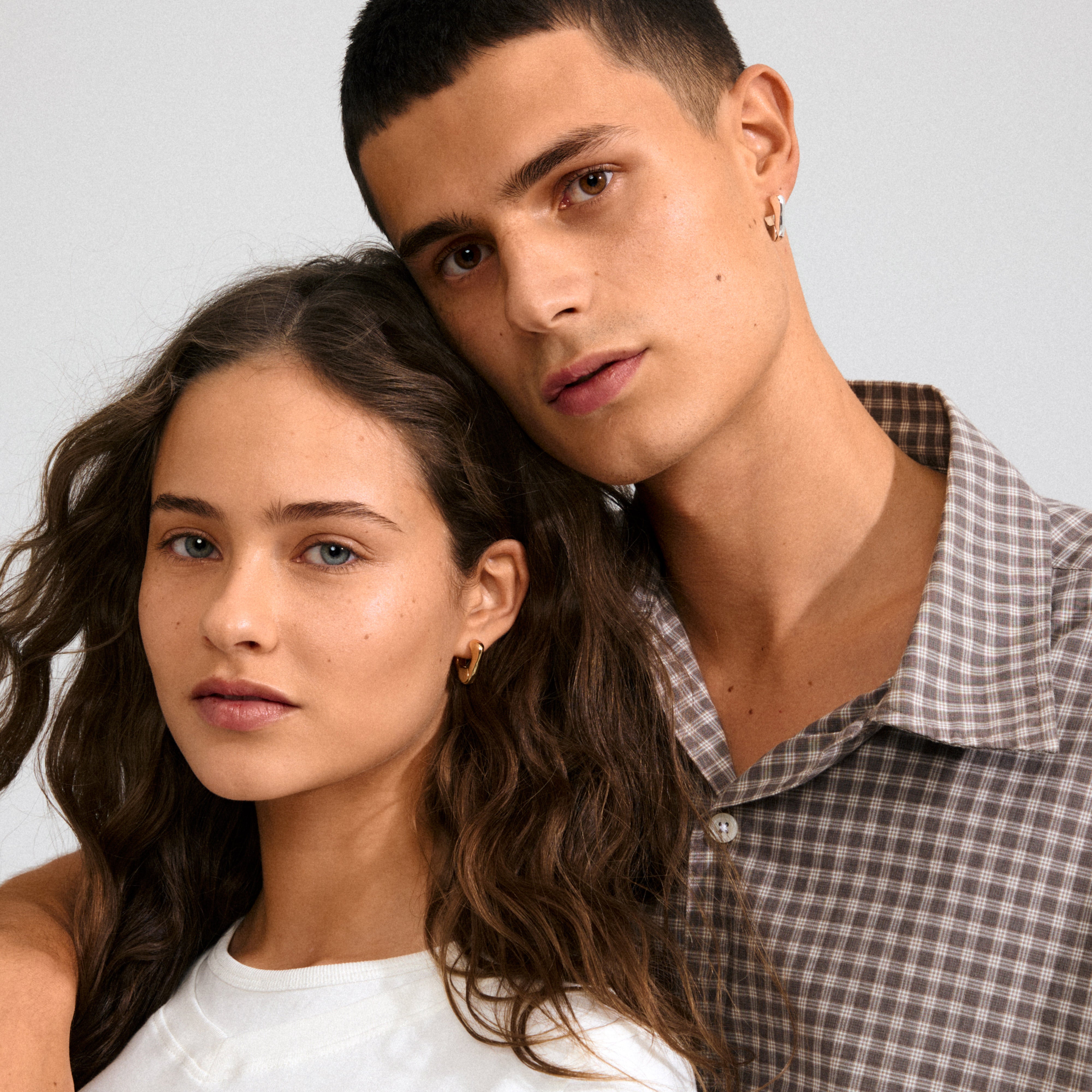 Two young adults, side by side, showcase Pilgrim's FREE earrings 168一分钟极速赛车--|实时赛果直播视频 gold-plated—small, organic-shaped hoops, embodying a simple yet elegant style.