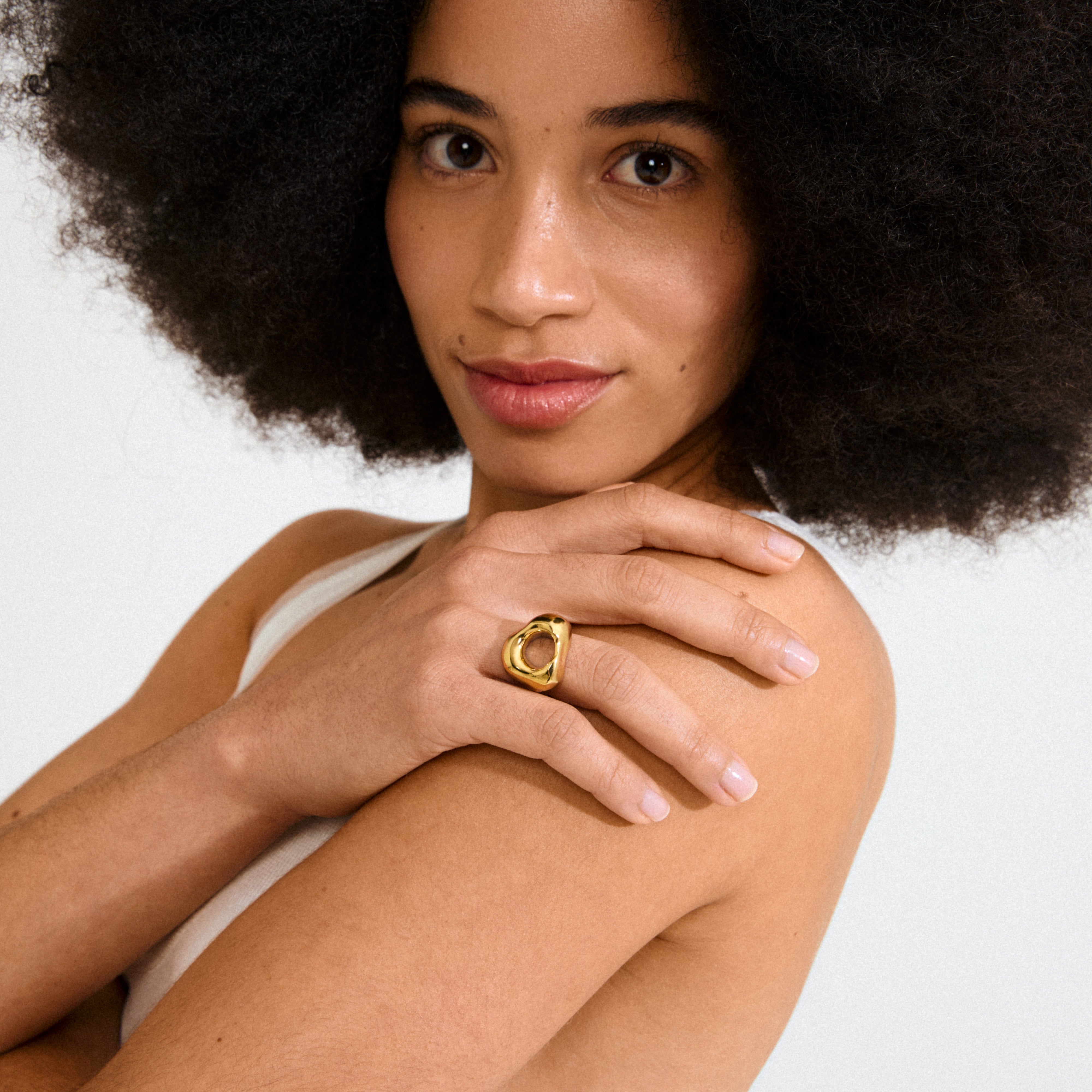 Young woman with an afro displays Pilgrim's FREE ring 168一分钟极速赛车--|实时赛果直播视频 gold-plated on her finger, showcasing its chunky, organic design in a minimalist, natural-lit setting.