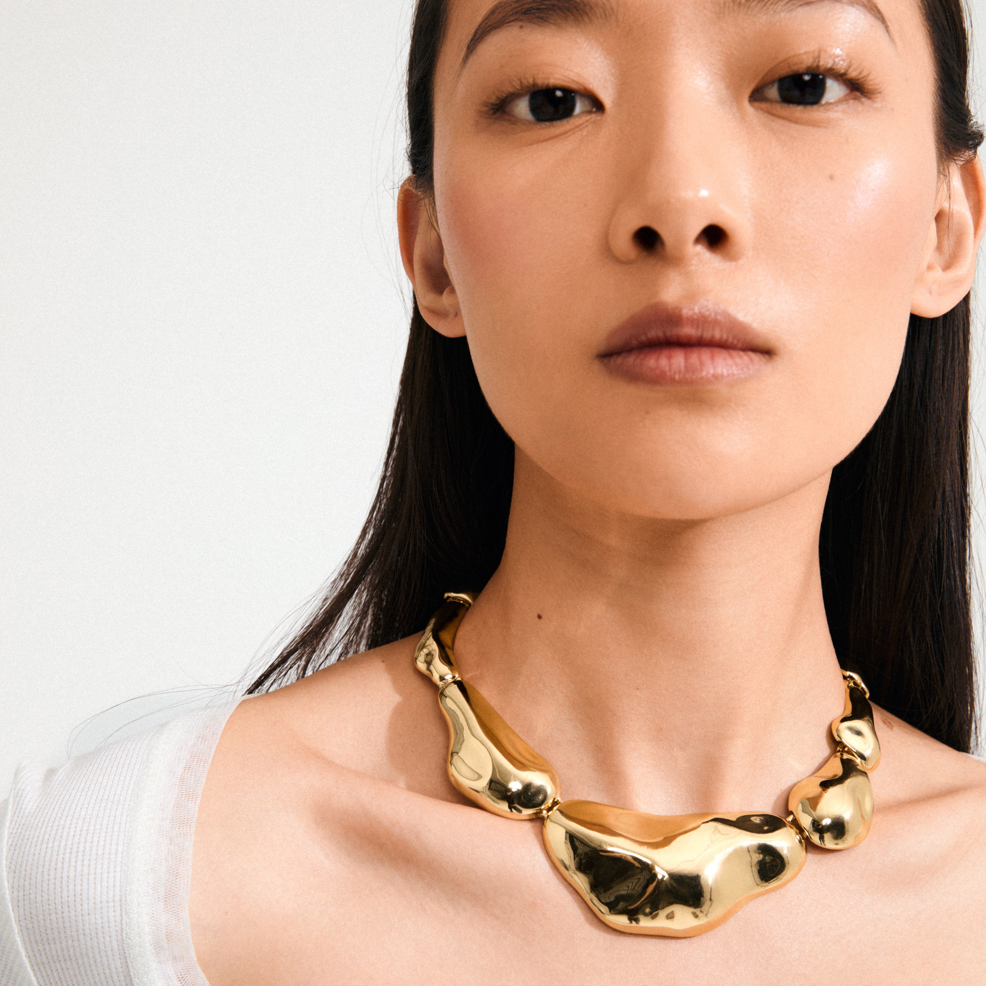 Young woman wearing Pilgrim's FREE statement necklace, a chunky 168一分钟极速赛车--|实时赛果直播视频 gold-plated piece with asymmetrical segments, capturing light and standing out as a stylish, recycled accessory.