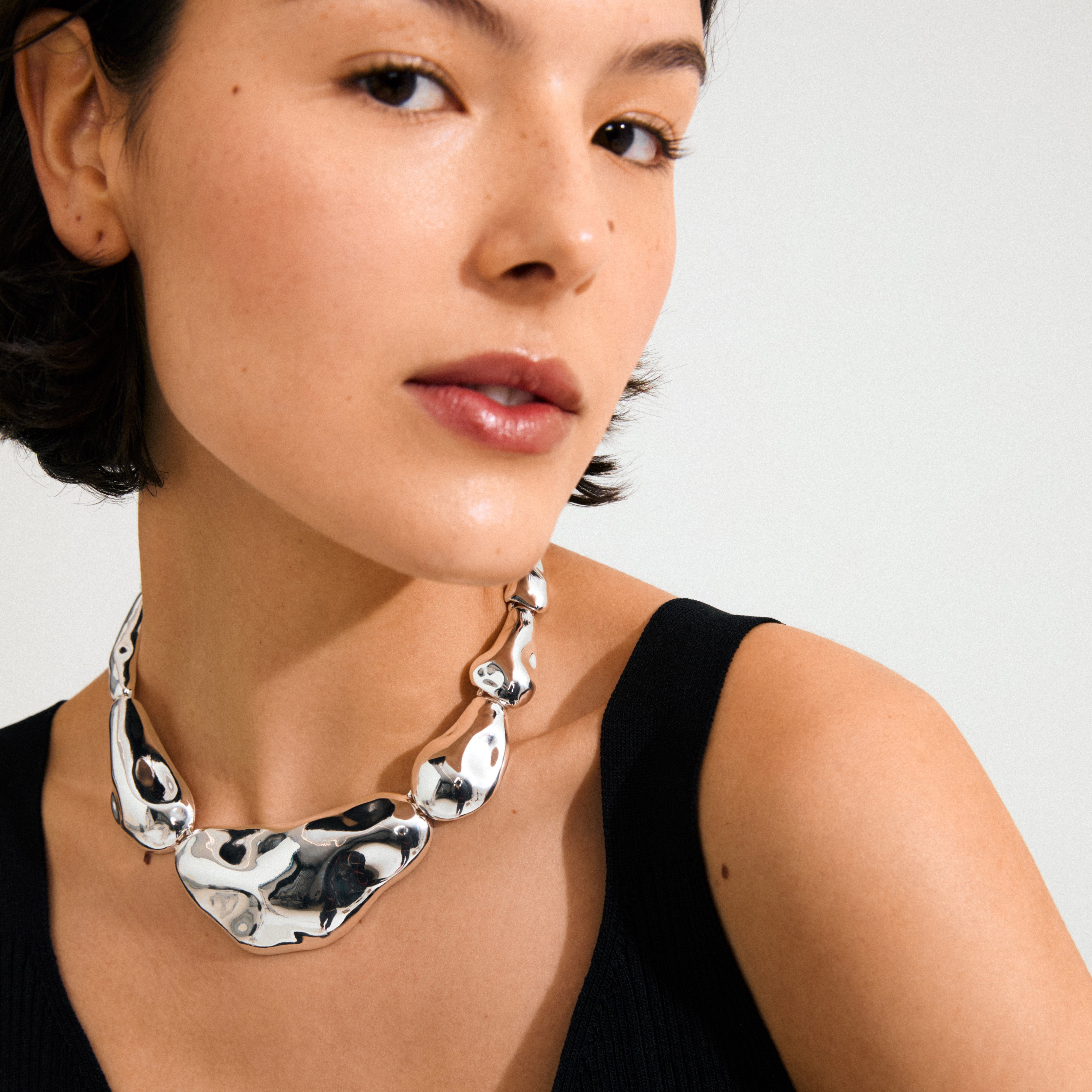Young woman wearing the FREE statement necklace silver-plated; chunky, asymmetrical, pebble-shaped links with a mirror finish, exuding a playful, ocean-inspired style.