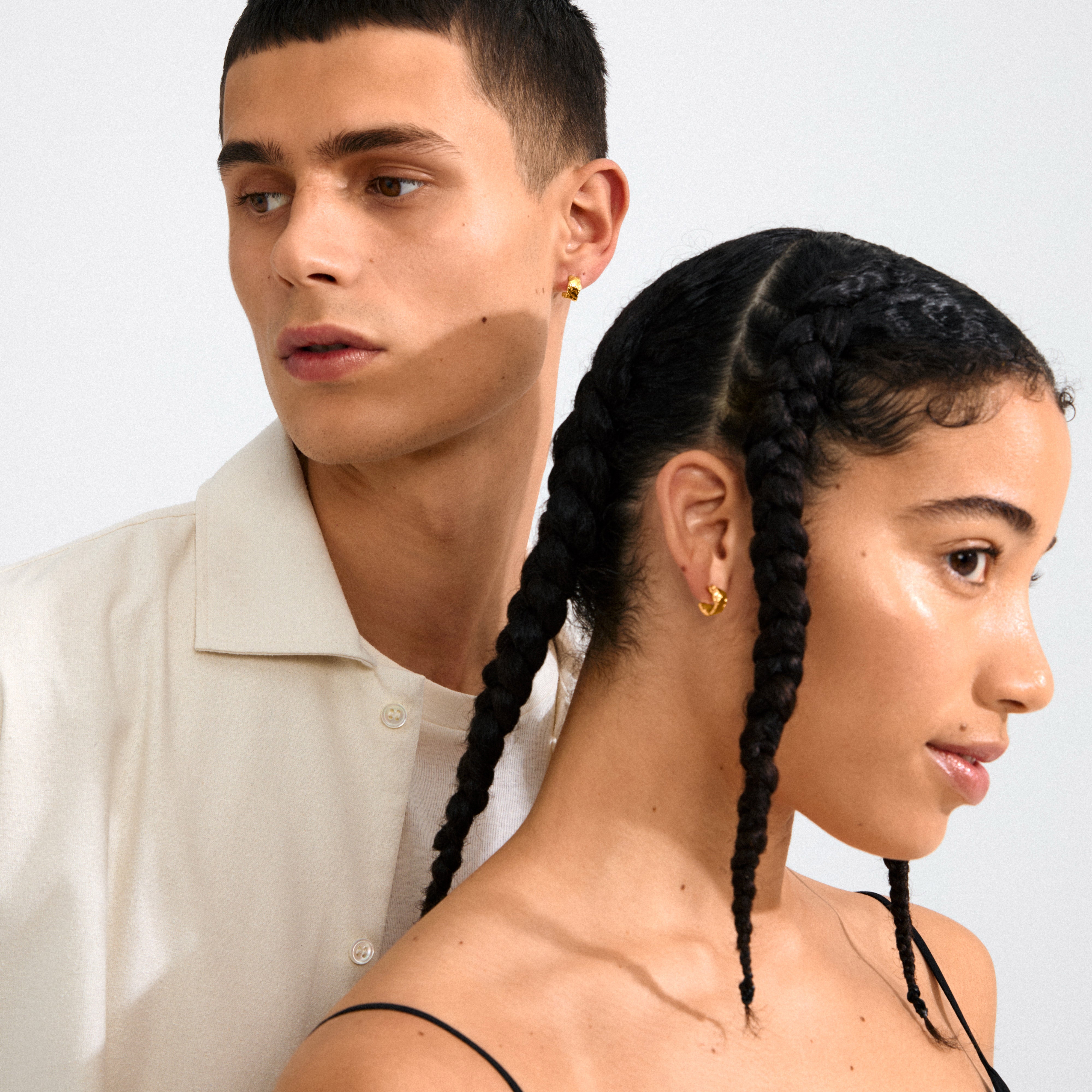 Two young adults showcase Pilgrim's INSTANT gold-plated huggie hoops, highlighting minimalist elegance with small, shiny semi-hoops perfect for everyday wear.