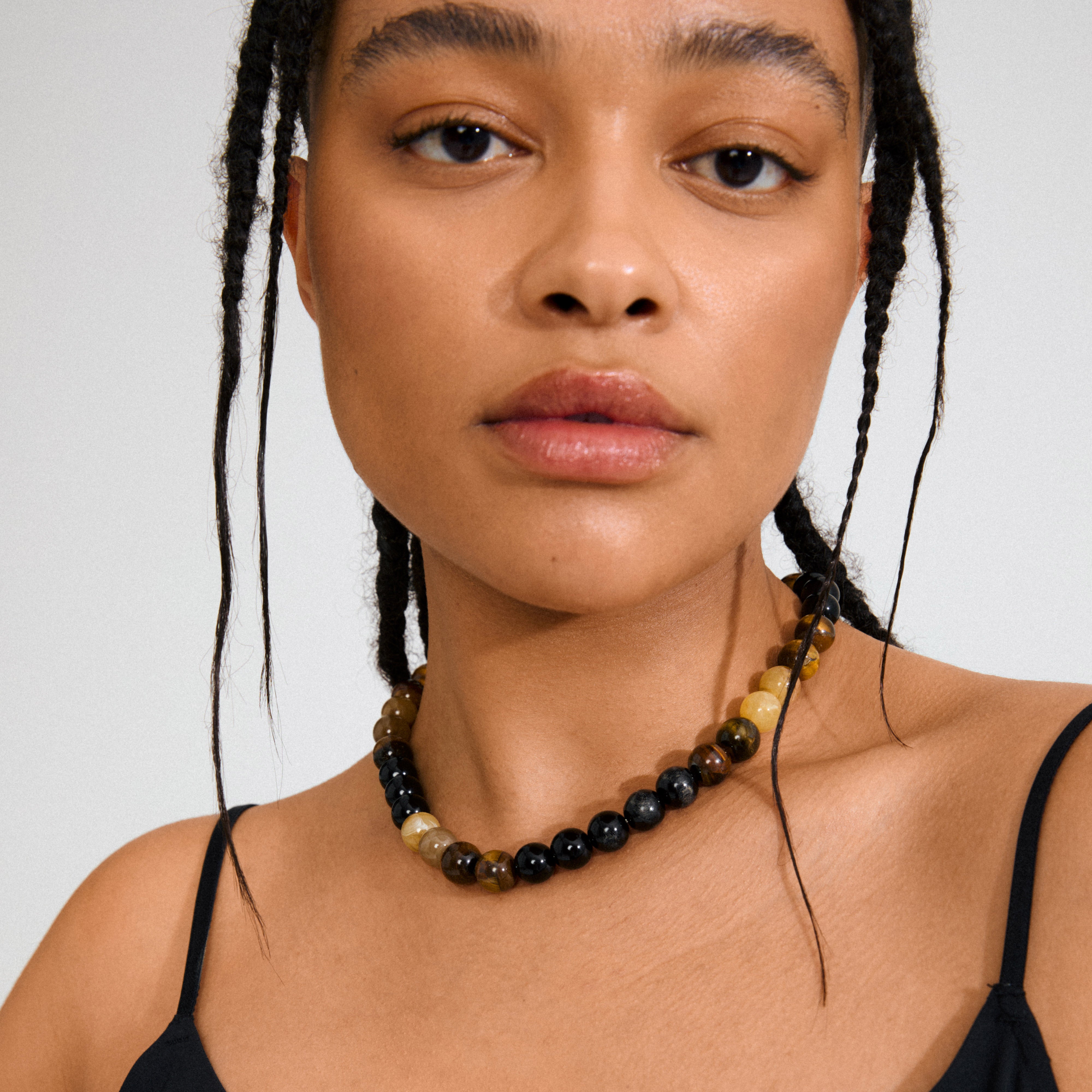 Model wearing the UNFOLD necklace gold-plated/brown with alternating Tiger Eye beads in black, brown, and honey-yellow, featuring a decorative gold-plated clasp.