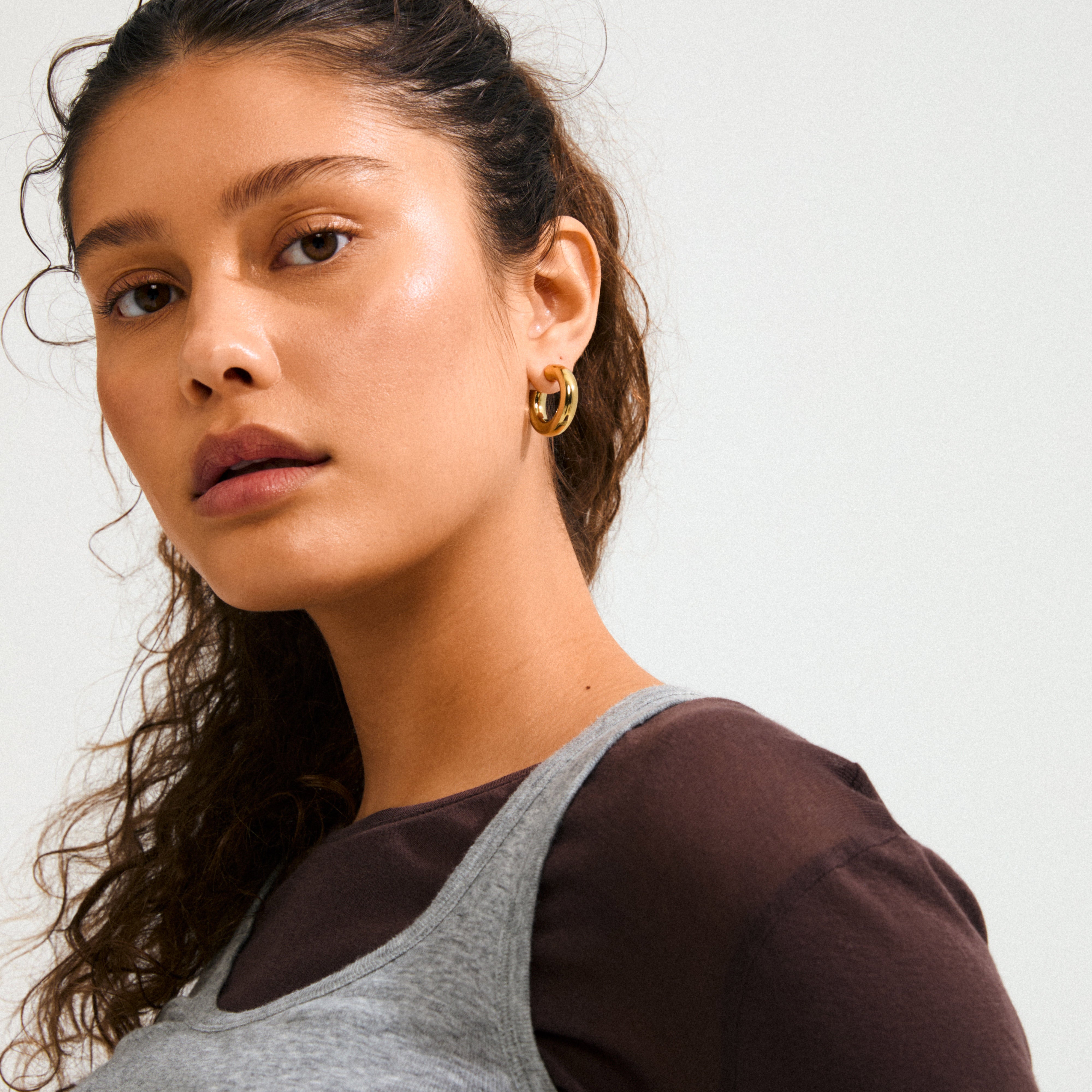Young woman wearing Pilgrim's PHASE medium gold-plated hoops, showcasing their chunky silhouette against her dark hair, embodying quiet luxury and timeless style.