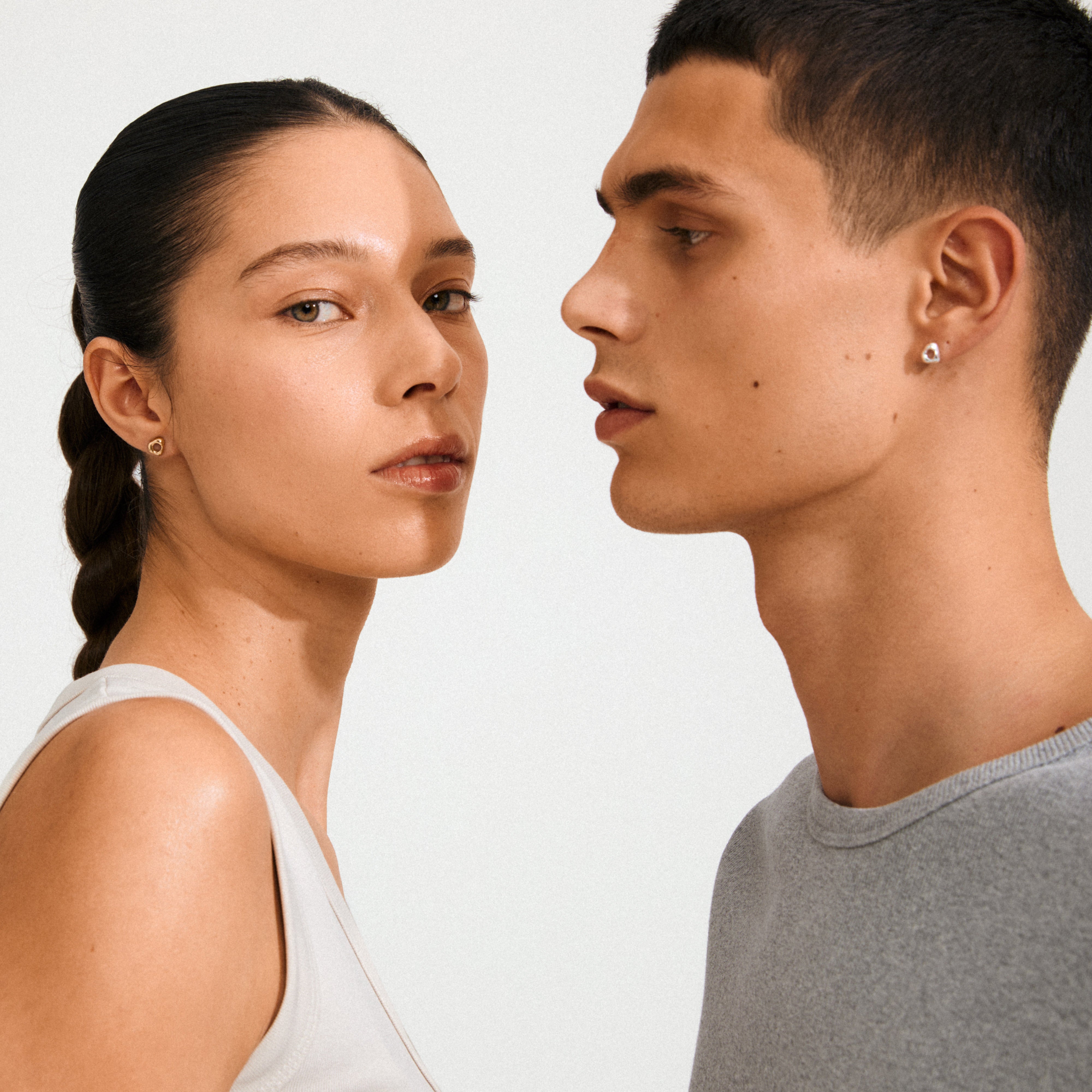 Two young adults showcasing Pilgrim's FREE 168一分钟极速赛车--|实时赛果直播视频 gold-plated stud earrings, highlighting their organic, minimalist design inspired by hagstones for everyday style.