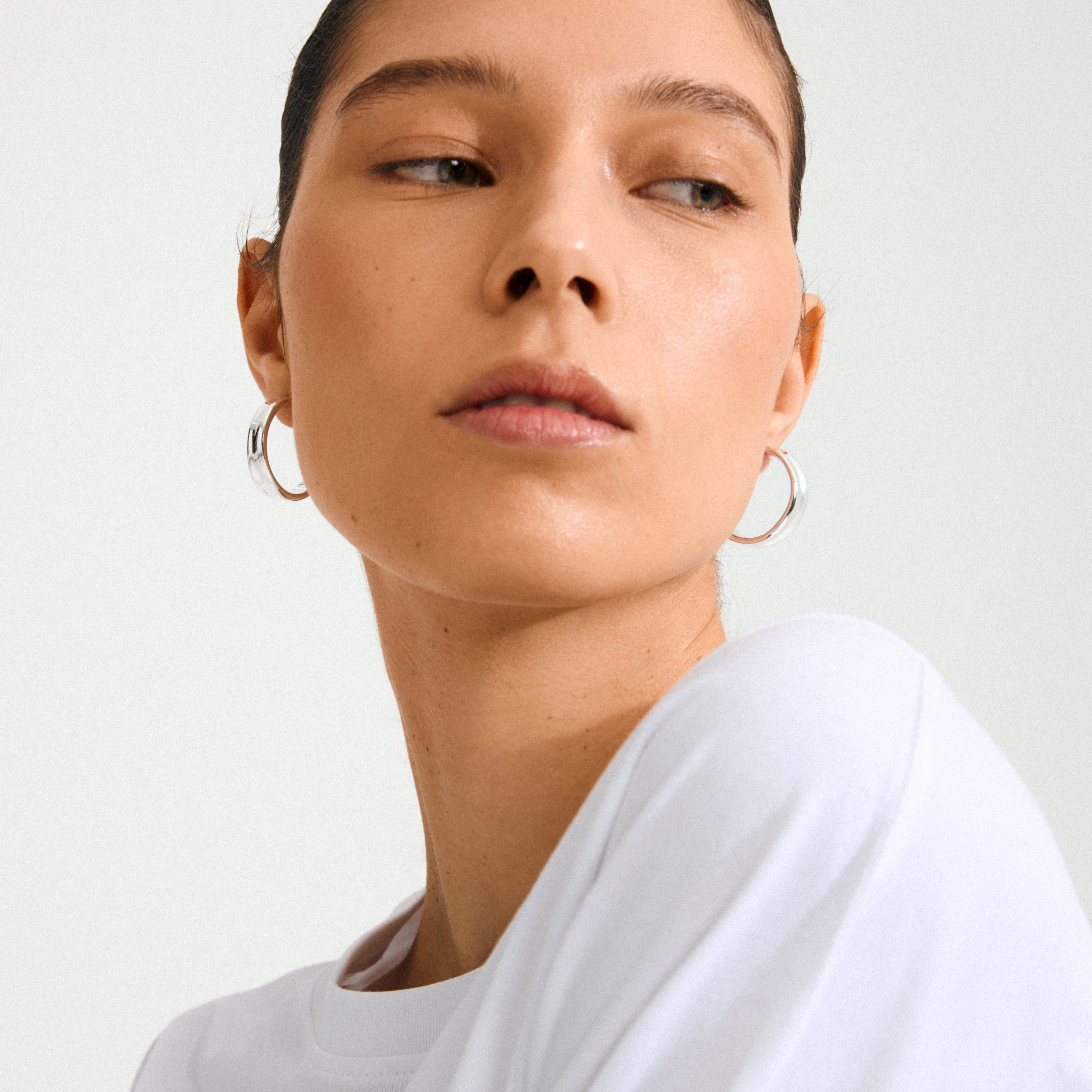 Young woman wearing KAYDEN hoops silver-plated, showcasing their bold, minimalist design and shiny finish, embodying Scandi coolness and eco-friendly style from Pilgrim.